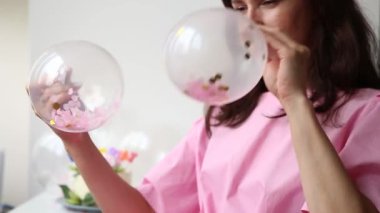 Beauty brunette girl waving two transparent air balloons with colorful confetti inside. Beautiful happy young woman on birthday holiday party. Joyful model having fun and and get ready to celebrating