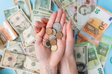 Kız, arka plandaki dağınık banknotlara karşı elinde bozuk para tutuyor. Uluslararası banknotlar - dolar, avro, bozuk para. Para işlemleri, krediler, döviz, kumar konsepti