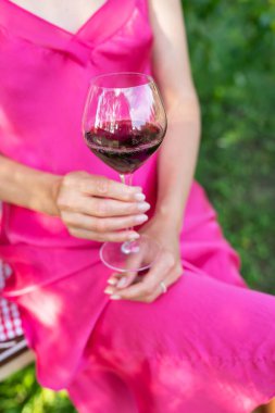 Pretty young woman in a pink dress holding a glass of red wine on a summer day. Summer outdoors holiday concept
