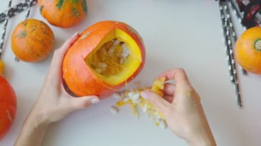 Girl preparing a scary pumpkin in autumn holidays. Woman making the Halloween attribute with your hands. Hands take out pumpkin seeds. Jack-O-Lantern creation. Do it yourself - creative realisation