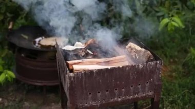 Firewood is burning in the grill in outdoor. Kindling firewood on a summer evening for barbecue. Wood logs are smoking in the metal brazier close up. White thick smoke rises from the roaster