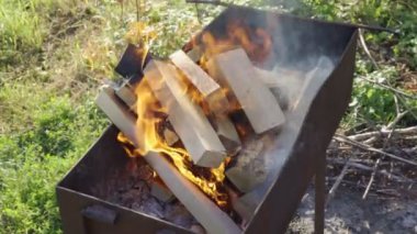 Firewood is burning in the grill in outdoor. Kindling firewood on a summer evening for barbecue. Wood logs are smoking in the metal brazier close up. White thick smoke rises from the roaster