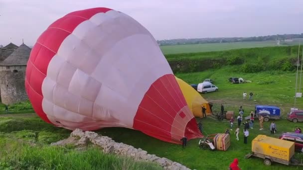 Kamianets Podilskyi ウクライナ 2021年5月14日 早朝に緑のフィールドに気球の空気充填のプロセス フェスティバル中のフライトの準備 離陸のための気球を準備する男たち — ストック動画