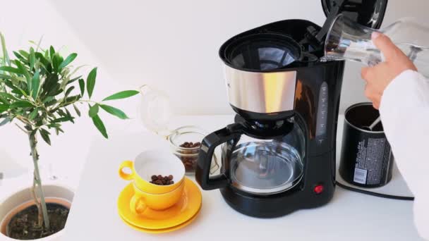 コーヒーを屋内で醸造するプロセス 女性の手は タンクに水を注ぎ 瓶からコーヒーを注ぎ ドリップコーヒーメーカーをオンにします 美しいインテリアでホームバリスタとして働く — ストック動画