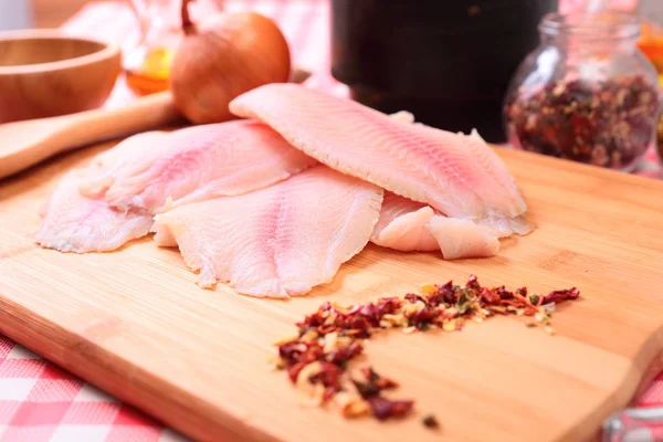 Tilapia de pescado crudo en tabla de cortar y especias —  Fotos de Stock