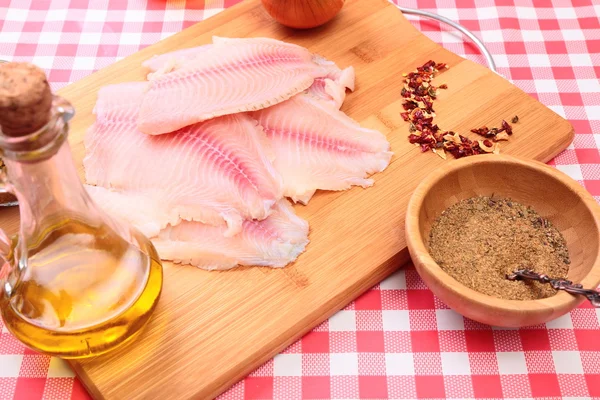 Tilapia de pescado crudo en tabla de cortar y especias —  Fotos de Stock