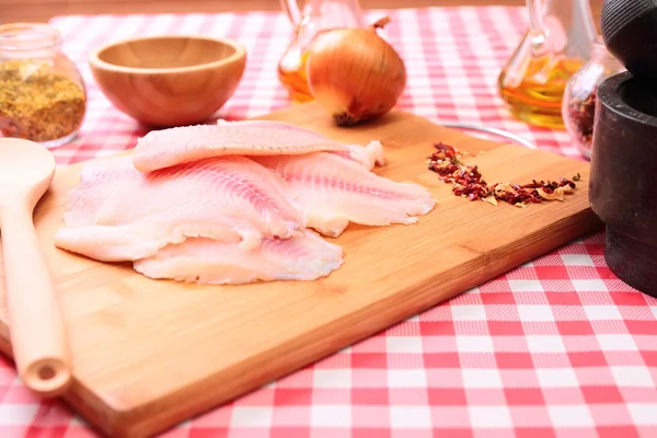 Tilapia de pescado crudo en tabla de cortar y especias —  Fotos de Stock