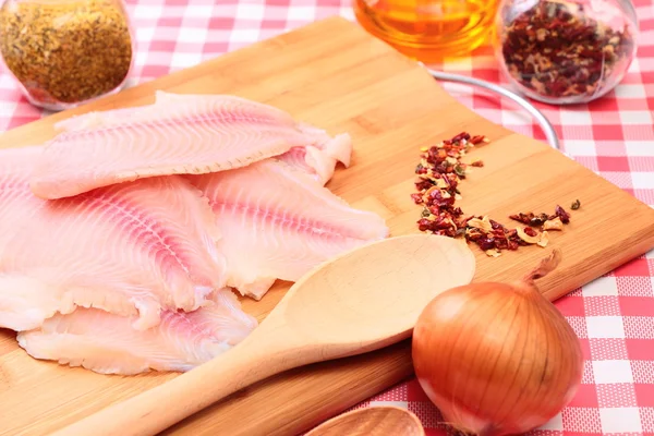 Tilapia de pescado crudo en tabla de cortar y especias —  Fotos de Stock