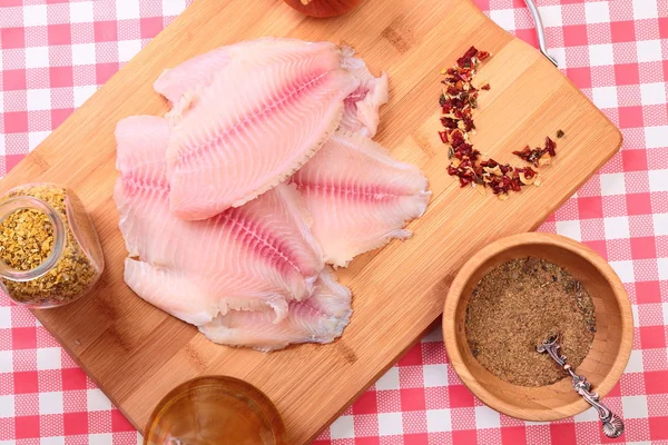 Tilapia de pescado crudo en tabla de cortar y especias —  Fotos de Stock