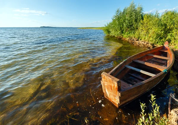 Zomer avond uitzicht op het meer met houten boot. — Stockfoto