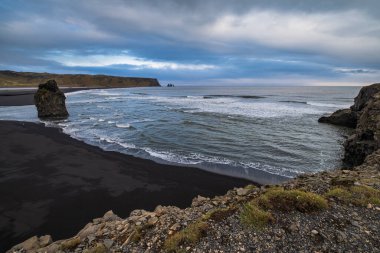 Reynisfjara Okyanusu 'nun siyah volkanik kumsal sahili ve Dyrholaey Burnu, Vik, Güney İzlanda' dan kaya oluşumları. Arkaplanda Reynisfjall Dağı.