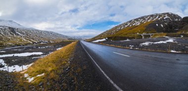 İzlanda 'da otomobil gezisi sırasında otoyol ve dağ manzarası. Manzaralı İzlanda manzarası: fiyortlar, tarlalar, bulutlar, buzullar, şelaleler.