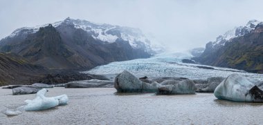 Buzul dili, İzlanda 'nın Orfajokull volkanı yakınlarındaki Vatnajokull buzulundan veya Vatna Buzulu' ndan kayar. Buzul gölü, buz blokları ve etrafındaki dağlarla. 