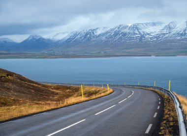 İzlanda 'da otomobil gezisi sırasında otoyol ve dağ manzarası. Manzaralı İzlanda manzarası: fiyortlar, tarlalar, bulutlar, buzullar, şelaleler.