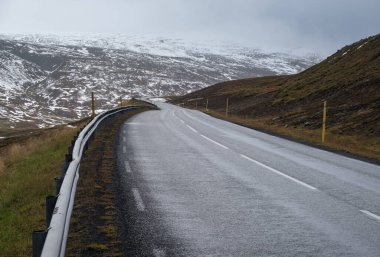 İzlanda 'da otomobil gezisi sırasında otoyol ve dağ manzarası. Manzaralı İzlanda manzarası: fiyortlar, tarlalar, bulutlar, buzullar, şelaleler.