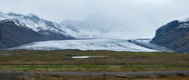 İzlanda 'da otomobil gezisi sırasında otoban manzarası. Manzaralı İzlanda manzarası: hamletler, dağlar, okyanus kıyıları, fiyortlar, tarlalar, bulutlar, buzullar, şelaleler.