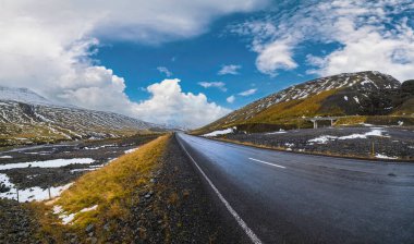 İzlanda 'da otomobil gezisi sırasında otoyol ve dağ manzarası. Manzaralı İzlanda manzarası: fiyortlar, tarlalar, bulutlar, buzullar, şelaleler.