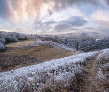 Kış geliyor. Sonbaharın sonlarına doğru, çimlerde, ağaçlarda ve yamaçlarda kırağı olan gündoğumu öncesi resimli bir manzara. Bulutlu gökyüzünden barışçıl güneş ışınları. Ukrayna, Karpat Dağları.