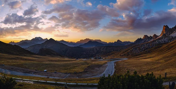 Sun glow in evening hazy sky. Italian Dolomites mountain silhouettes panoramic peaceful view from Giau Pass. Climate, environment and travel concept scene. Cars unrecognizable.