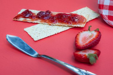 Krakerler ve taze çilek reçeli kırmızı arka planda izole edilmiş.