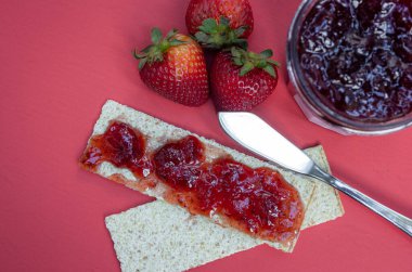 Krakerler ve taze çilek reçeli kırmızı arka planda izole edilmiş.