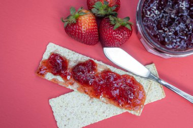 Krakerler ve taze çilek reçeli kırmızı arka planda izole edilmiş.