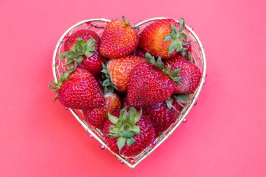 Beyaz arka planda kalp şeklinde bir sepetin içindeki parlak kırmızı çilekler.