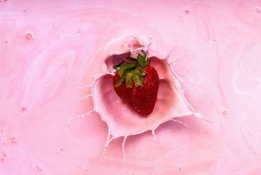 Pembe krema kasesine sıçrayan çileğin aksiyon görüntüsü.