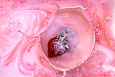 Pembe krema kasesine sıçrayan çileğin aksiyon görüntüsü.