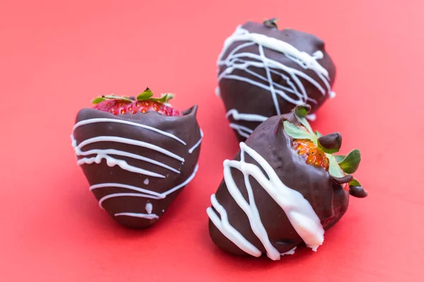 チョコレートで覆われたイチゴに赤い背景に白いチョコレートの渦が — ストック写真