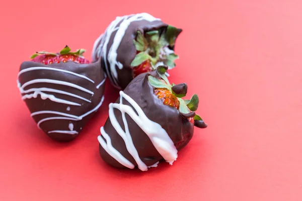 チョコレートで覆われたイチゴに赤い背景に白いチョコレートの渦が — ストック写真