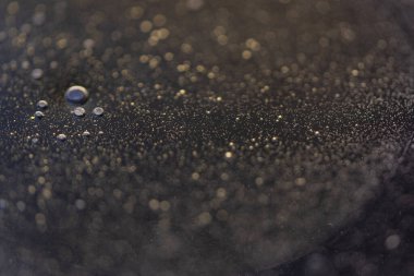 Suyun üstünde baloncuklu yağ damlası, koyu bir arka plan ile makro.