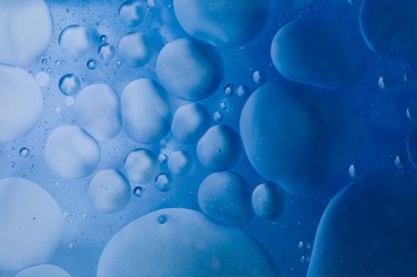 Suyun üzerinde mavi arkaplanı soyut olarak yüzen makro zeytinyağı damlaları