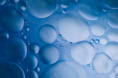 Suyun üzerinde mavi arkaplanı soyut olarak yüzen makro zeytinyağı damlaları