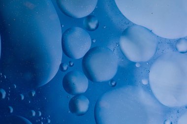 Suyun üzerinde mavi arkaplanı soyut olarak yüzen makro zeytinyağı damlaları