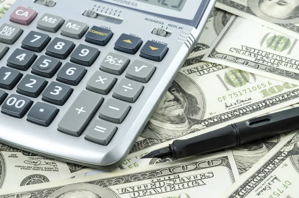 Caneta e calculadora em um fundo de notas de dólar americano — Fotografia de Stock