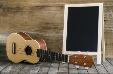 Ukulele gitar ve ahşap zemin üzerinde boş yazı tahtası