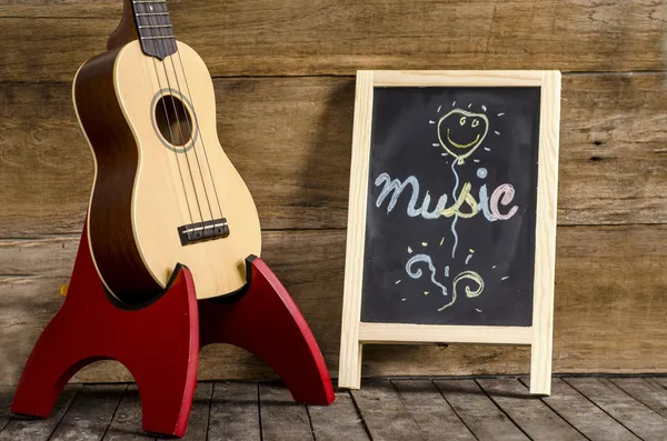 Ukelele gitaar en bord met het woord "muziek" geschreven op houten achtergrond — Stockfoto