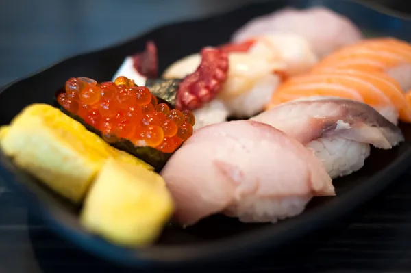 Close up of Ikura suhi in chopsticks and Variety Sushi Set on Black Dish — Stock Photo, Image