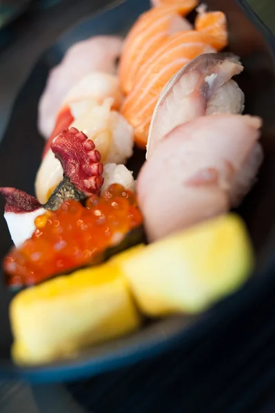 Close up of Ikura suhi in chopsticks and Variety Sushi Set on Black Dish — Stock Photo, Image