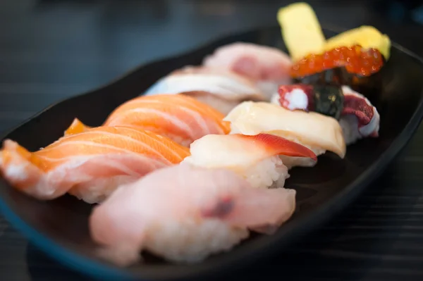 Close up of Ikura suhi in chopsticks and Variety Sushi Set on Black Dish — Stock Photo, Image
