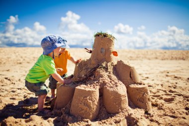 Two boys building large sandcastle on the beach clipart