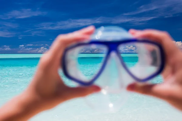 Mão segurando óculos de snorkel contra praia e céu — Fotografia de Stock