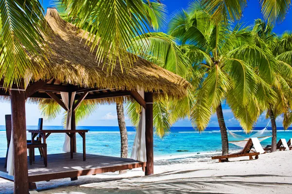 Беседка со стульями на пустынном пляже с пальмами — стоковое фото
