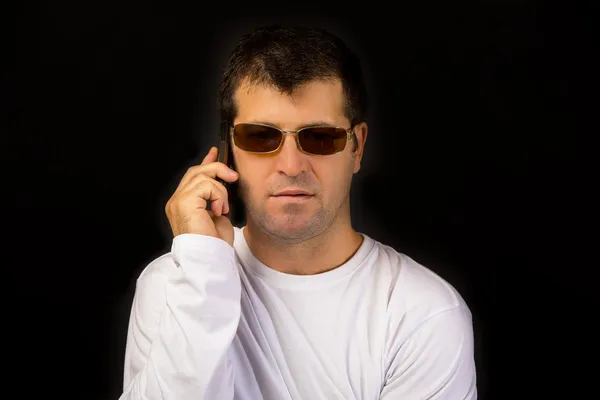 Hombre con gafas de sol hablando por teléfono sobre fondo negro —  Fotos de Stock