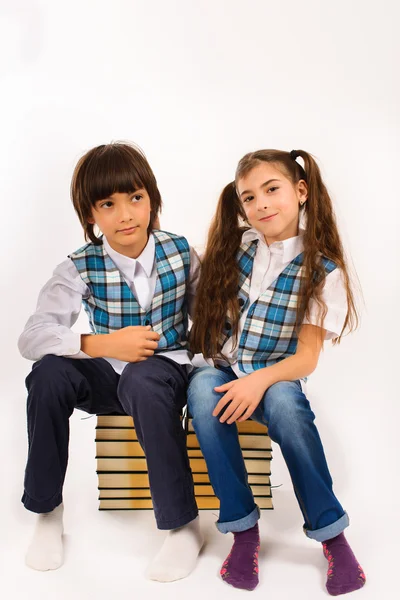 Belle fille et un garçon assis sur une pile de livres — Photo