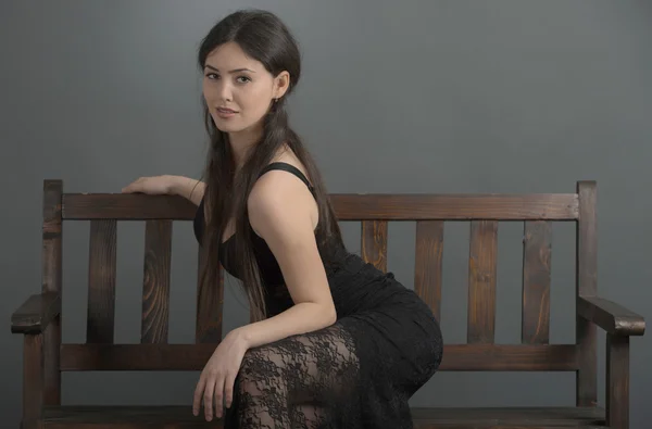 Beautiful woman in elegant dress posing in studio sitting on ben — Stock Photo, Image