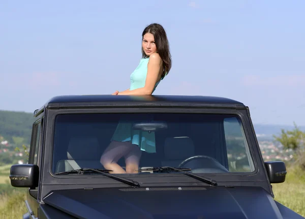 Feliz joven mujer saliendo del techo solar del coche — Foto de Stock