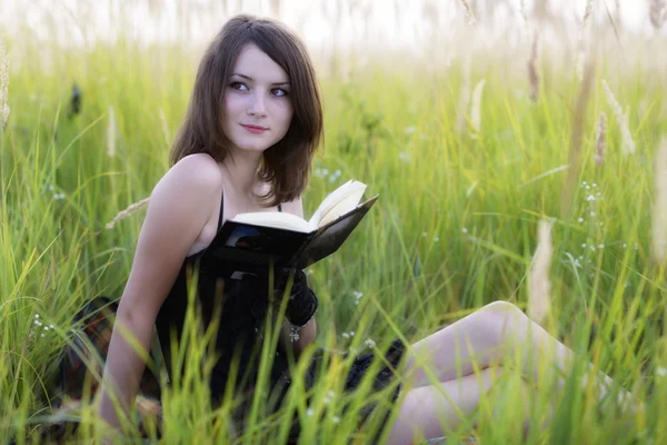 A menina sentada em uma grama, lendo um livro — Fotografia de Stock