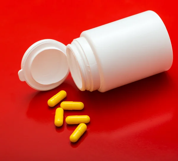 White tube of yellow pills isolated on red background — Stock Photo, Image